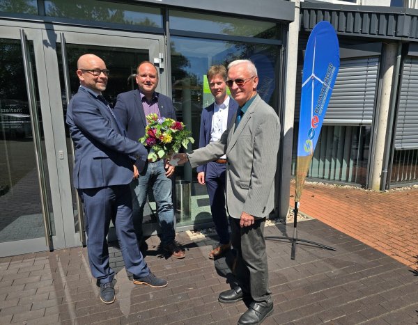 !B Aufsichtsratsvorsitzender überreicht neuem Geschäftsführer Blumenstrauß, im Hintergrund stehen der alte Geschäftsführer und Bürgermeister